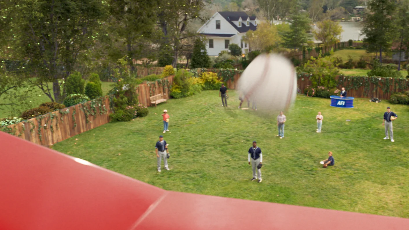 A baseball flies over a shiny red roof. A backyard in the background.