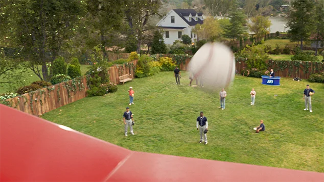 A baseball flies over a AFI's shiny red roof. A backyard in the background.