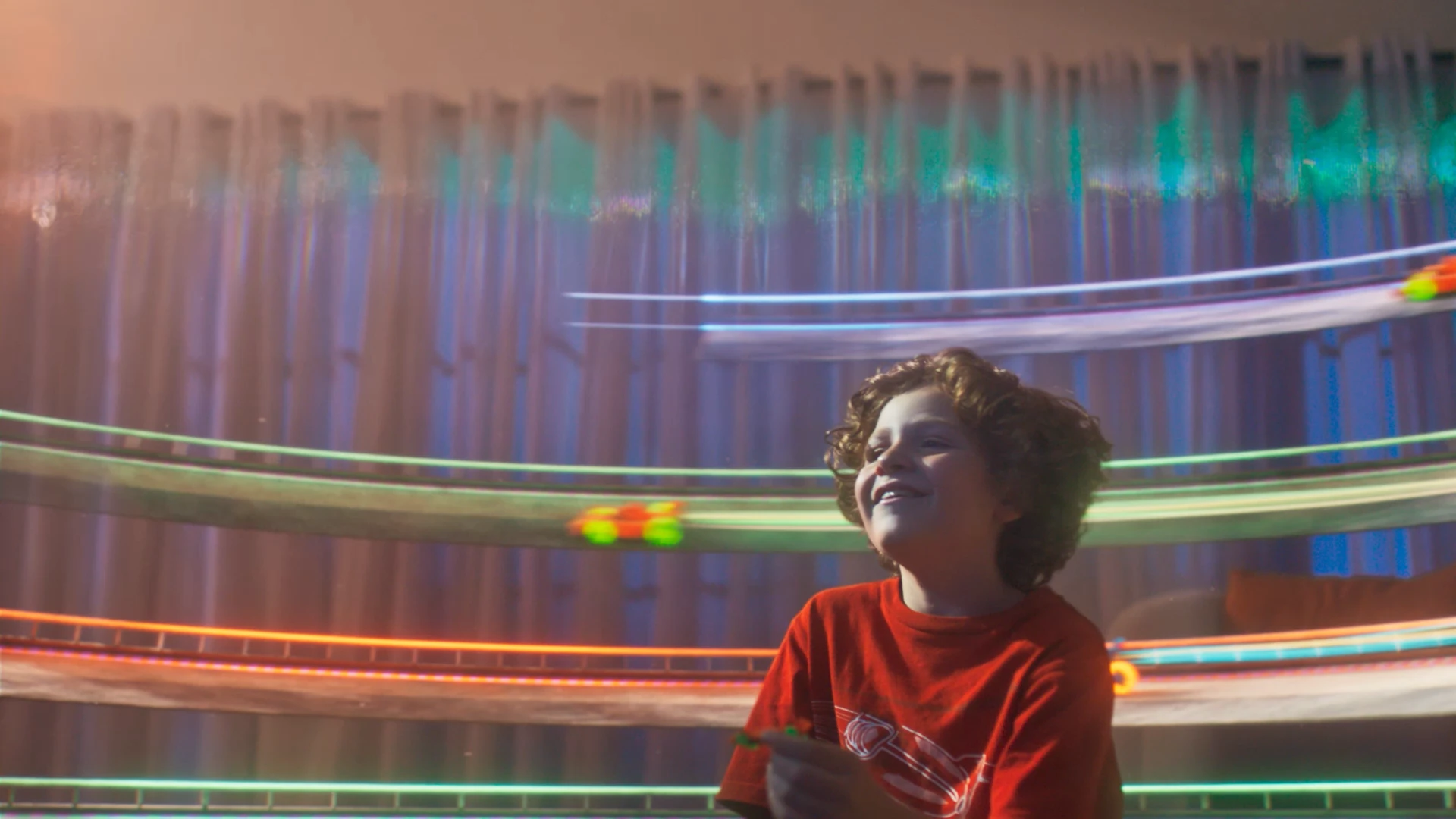 A kid looks around his living room as a race track filled with colorful cars appears around him.