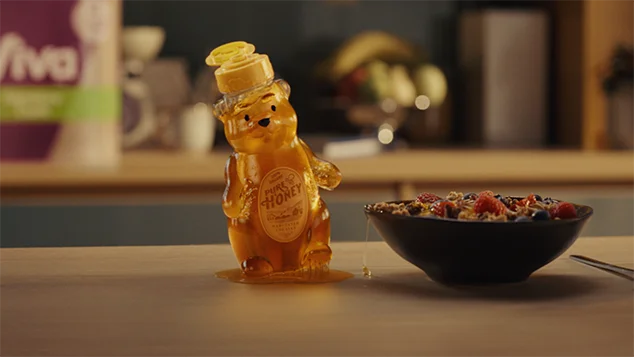 The honeybear bottle is moving in a puddle of sticky honey.