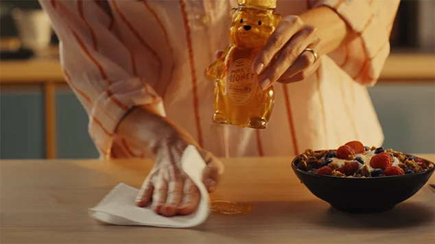 A real woman picks up the CG honeybear bottle, as she wipes the table with Viva paper towels.