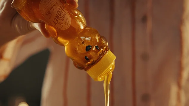 The  woman squeezes the honey out of the surprised honeybear bottle.